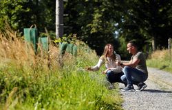 Ein Paar kniet und betrachtet die Vegetation am Wegesrand im Naturpark Geras.