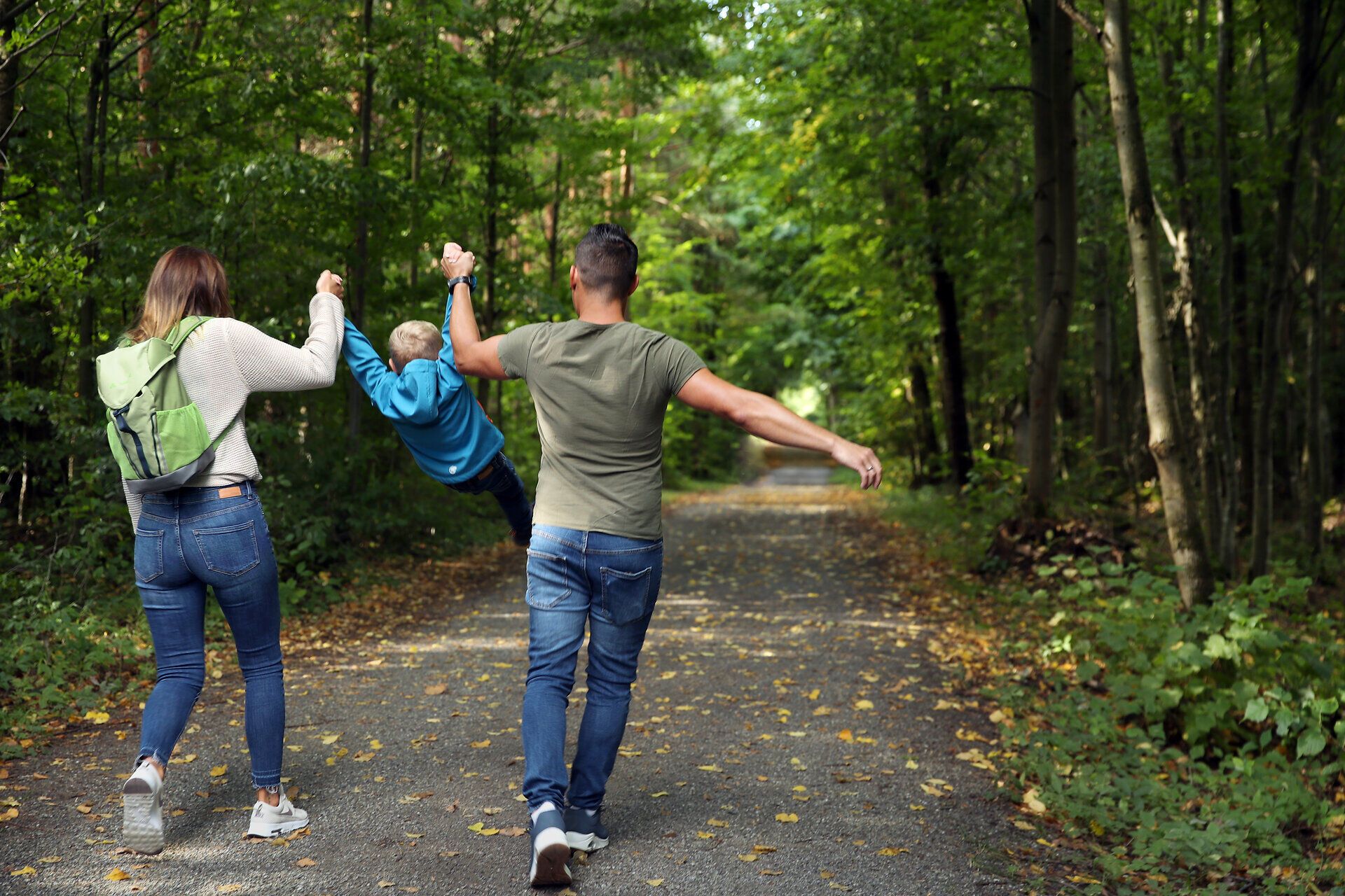 Eine Familie spaziert entlang eines Weges mitten durch den Wald. 